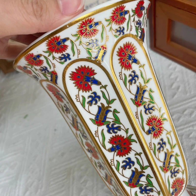 Vase en porcelaine, petit format sobre pour bureau Nesty, gros plan sur le bord du vase et ses médaillons floraux rouges, bleus et dorés, tenu à la main
