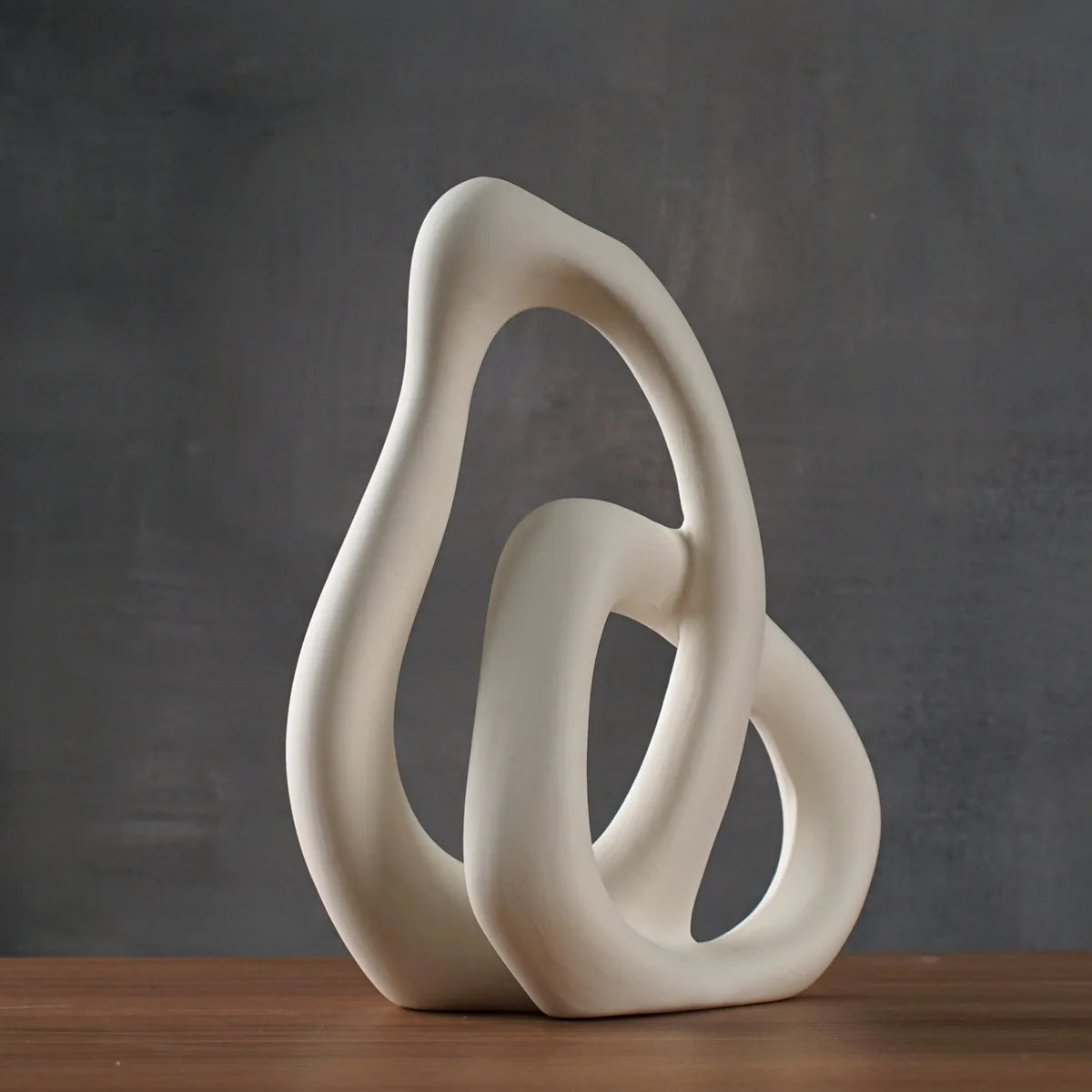 Vase en céramique abstrait Nesty - Modèle blanc en forme de boucles entrelacées, sur table en bois, fond sombre
