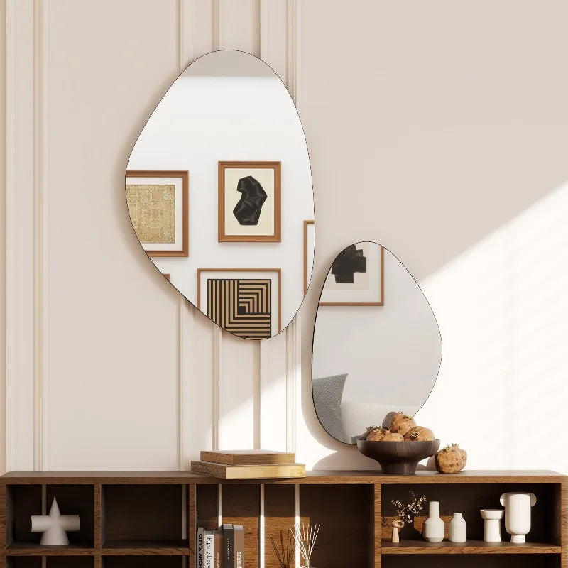 Duo de miroirs galets asymétriques à cadre noir fin, au-dessus d'un meuble bas avec livres et coupe de grenades - Nesty