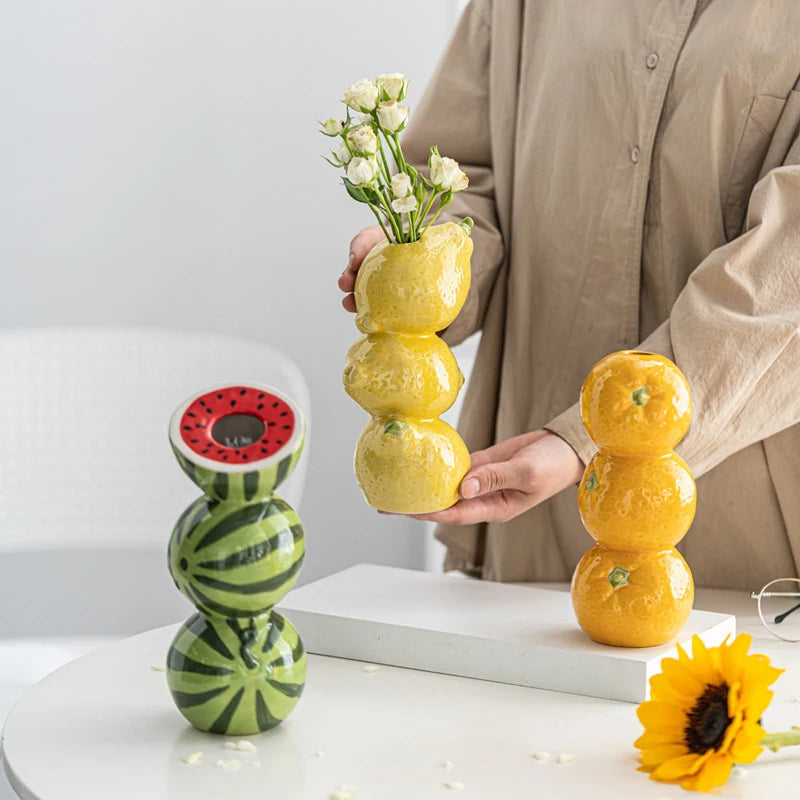 Coupelle-vase en céramique — fruits, fleurs ou bougie - Nesty - Trio de vases en relief pastèque verte, citron jaune et mandarine orange sur table blanche, le vase citron tenu à la main avec des roses blanches