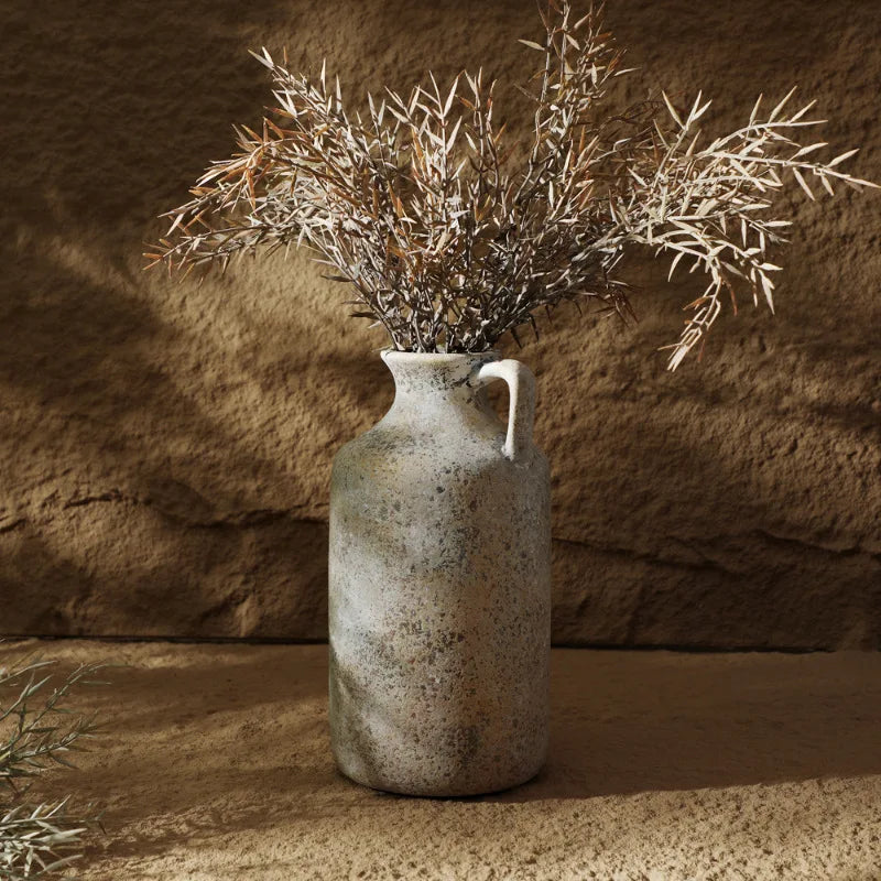 Vase en céramique style wabi-sabi pour fleurs séchées Nesty, cruche seule, garnie de branches séchées brun-argenté, devant un mur en pierre