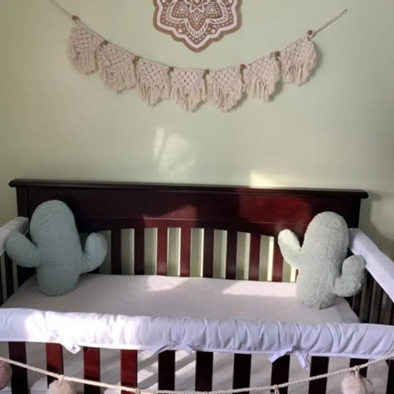 Tenture macramé à franges à tissage bohème Nesty, guirlande accrochée au-dessus d'un lit de bébé avec coussins en forme de cactus