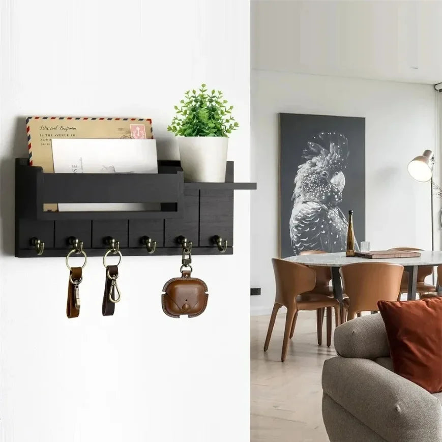 Porte-clés mural en bois avec étagère Nesty, version noire installée dans un salon avec tableau de perroquet et salle à manger en fond