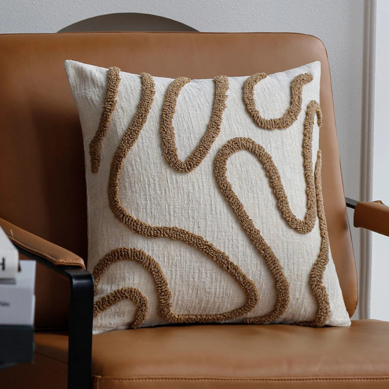 Housse de coussin en chénille tuftée, lignes simples Nesty, coussin en chénille écrue à motif tufté sinueux beige, posé seul sur fauteuil en cuir près de livres