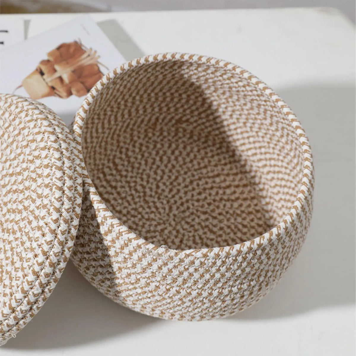 Petit panier rond tressé en corde de coton avec couvercle Nesty, vue en angle du panier ouvert et de son couvercle, magazine culinaire en arrière-plan