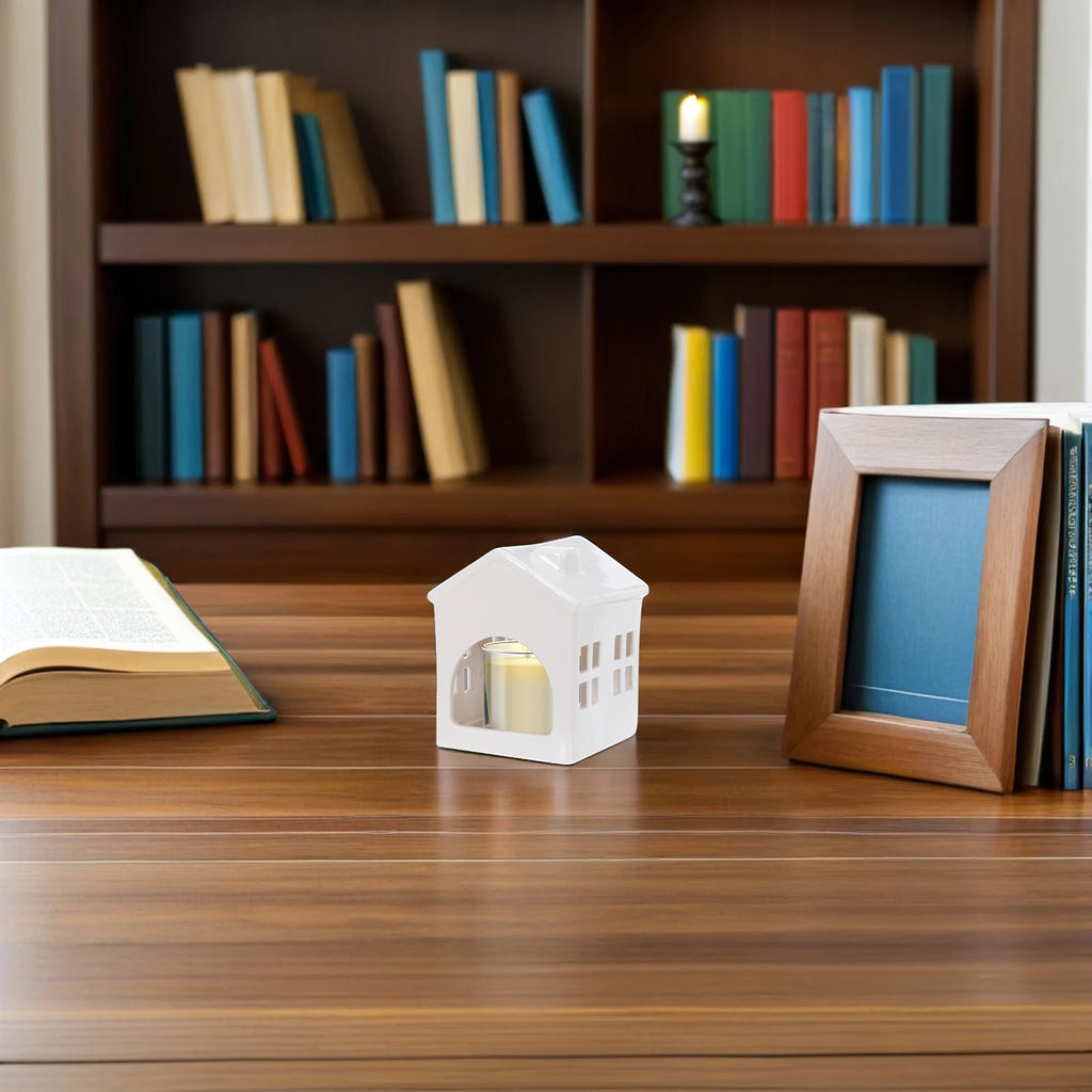 Photophore céramique blanc forme maisonnette avec bougie allumée à l'intérieur, sur bureau devant une bibliothèque - Nesty