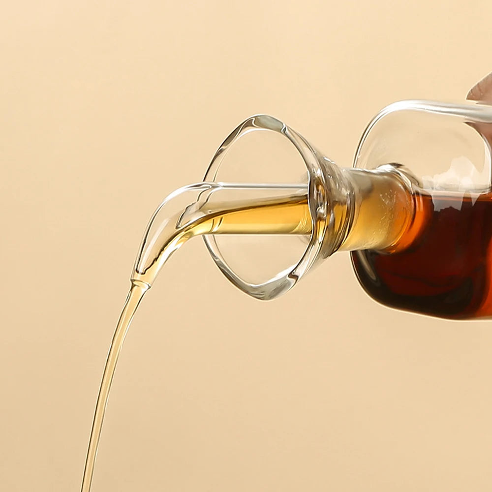 Burette à huile d'olive en verre borosilicate, anti-goutte Nesty, gros plan sur le bec verseur d'une burette en verre en train de verser un filet d'huile dorée
