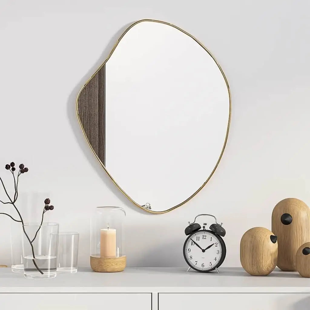 Miroir mural doré Nesty - Accroché au mur au-dessus d'une console blanche avec réveil et bougie