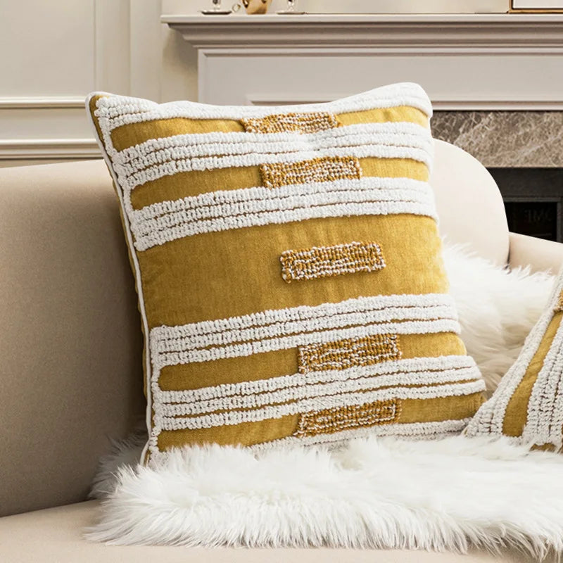 Housse de coussin bouclette à broderie géométrique bohème Nesty, coussin jaune moutarde à rayures bouclette blanches sur un canapé beige devant une cheminée