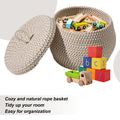 Petit panier rond tressé en corde de coton avec couvercle Nesty, panier ouvert garni de circuit de train en bois et de cubes alphabet, texte en anglais cozy and natural rope basket