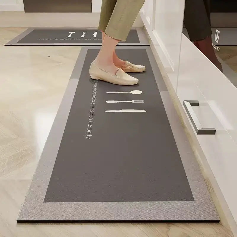 Tapis de cuisine long gris à motif de couverts illustrés, posé au sol devant des meubles de cuisine blancs, avec une personne debout dessus.