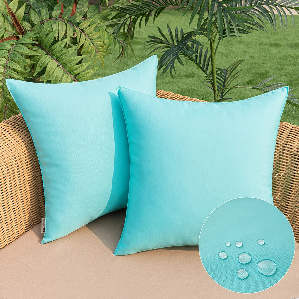 Housses de coussin extérieur imperméables, lot de 2 Nesty, deux housses turquoise posées sur un canapé en rotin, zoom sur les gouttes d'eau imperméabilisantes