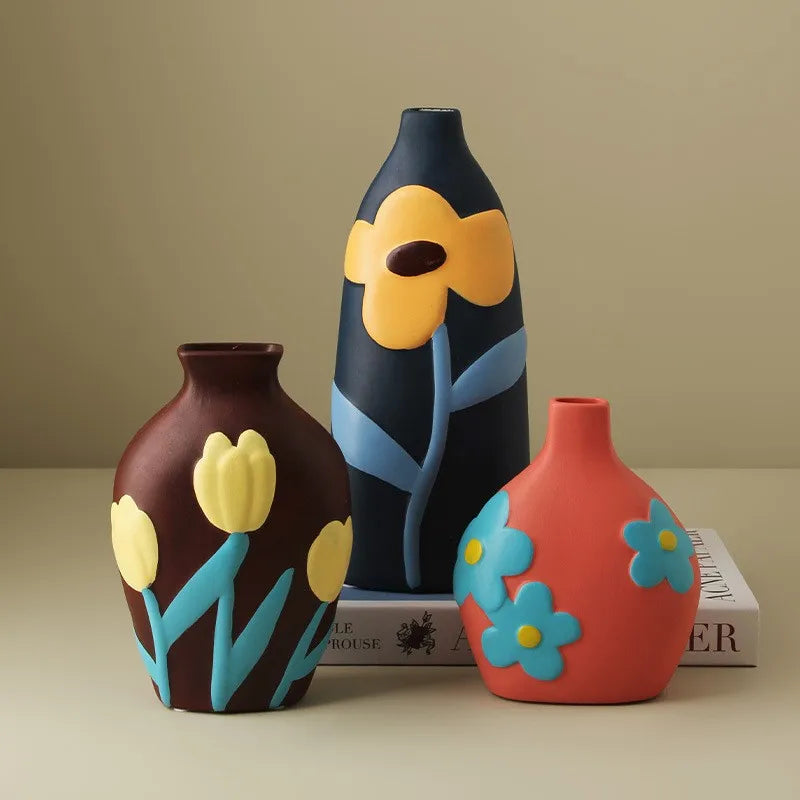 Vase céramique émaillé teintes Morandi, style nordique - Nesty - Trois vases peints marron à tulipes jaunes, bleu marine à fleur orange et corail à fleurs bleues, posés sur un livre