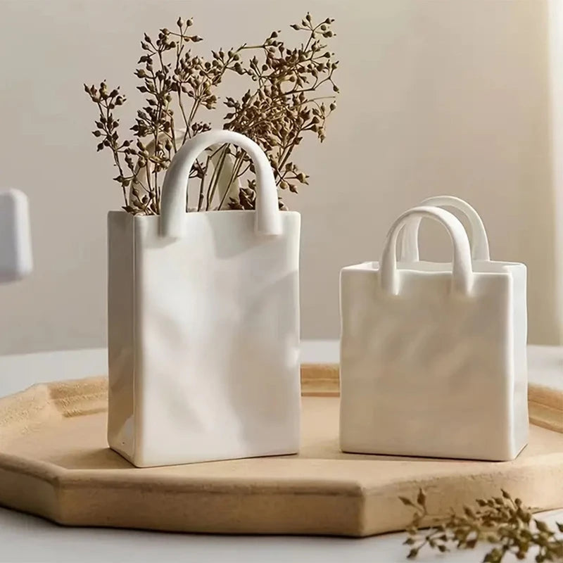 Vase blanc forme sac à main, fleurs séchées - Nesty - Deux tailles avec brins de fleurs séchées brunes, sur un plateau en bois près d'un verre et d'une bougie