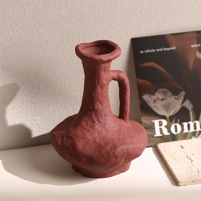 Vase céramique artistique, style nordique rétro - Nesty - Vase bordeaux à anse sculpturale et forme libre, posé sur une étagère près d'un magazine