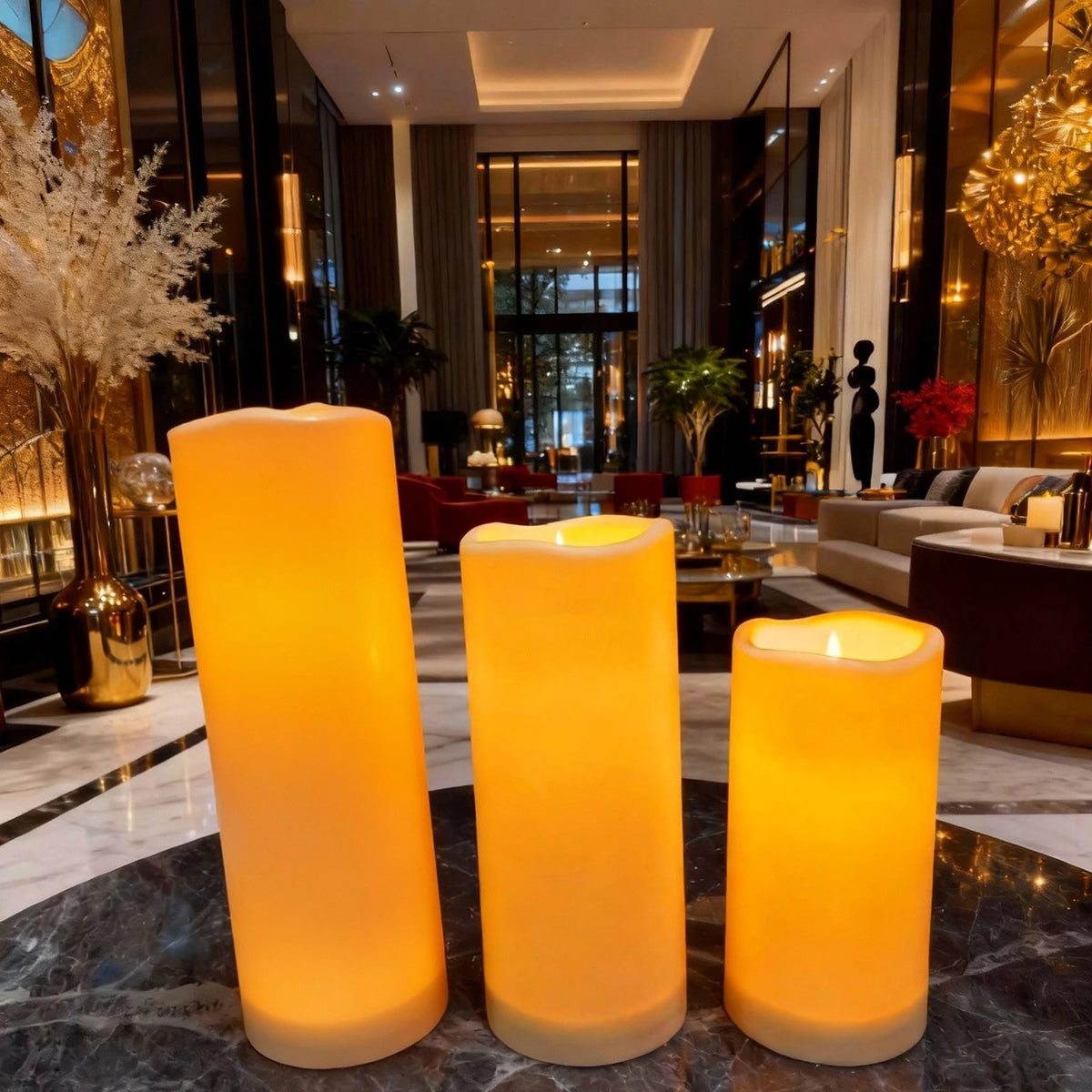 Bougies LED pilier vacillantes, télécommande, intérieur et extérieur Nesty, trois bougies LED pilier de tailles différentes, lumière ambrée, dans un hall d'entrée moderne avec plantes et lustres dorés