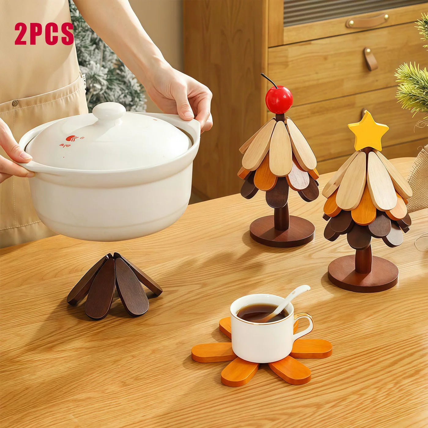 Dessous de plat en bois pliable forme fleur, en position dépliée sous une cocotte et une tasse, à côté de deux figurines sapin de Noël décoratives - Nesty