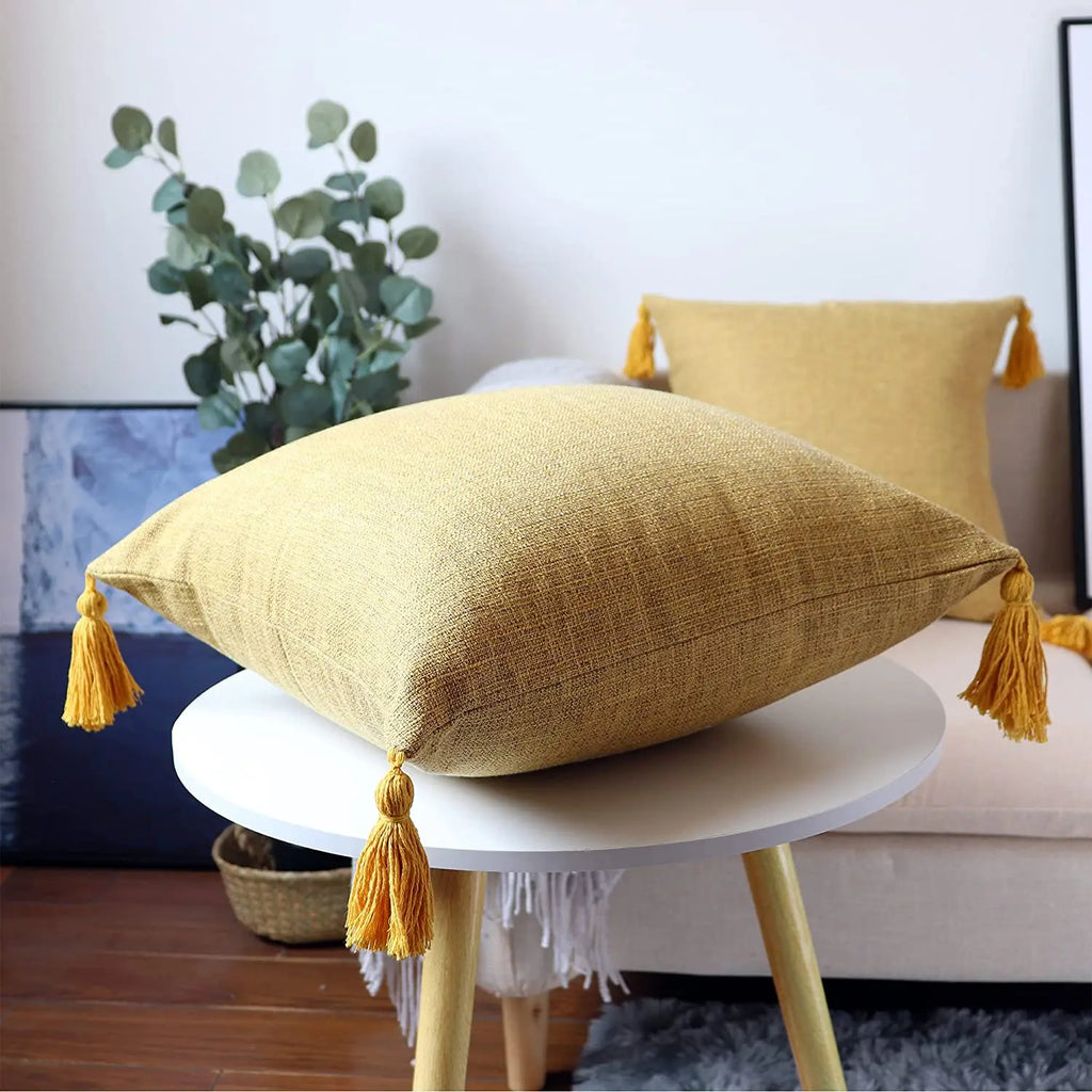 Housse de coussin en lin avec pompons, toutes saisons Nesty, housses de coussin jaune moutarde à pompons assortis, posées sur canapé et table d'appoint blanche