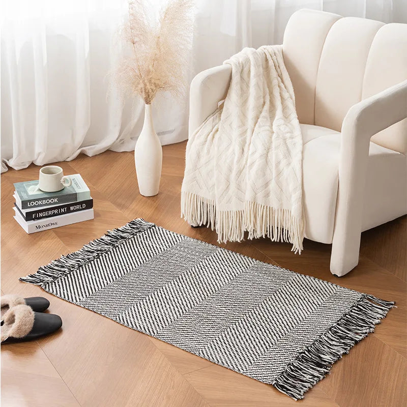 Tapis tressé en coton et lin — franges - Nesty, variante à motif chevrons noir et blanc, posée près d'un fauteuil crème