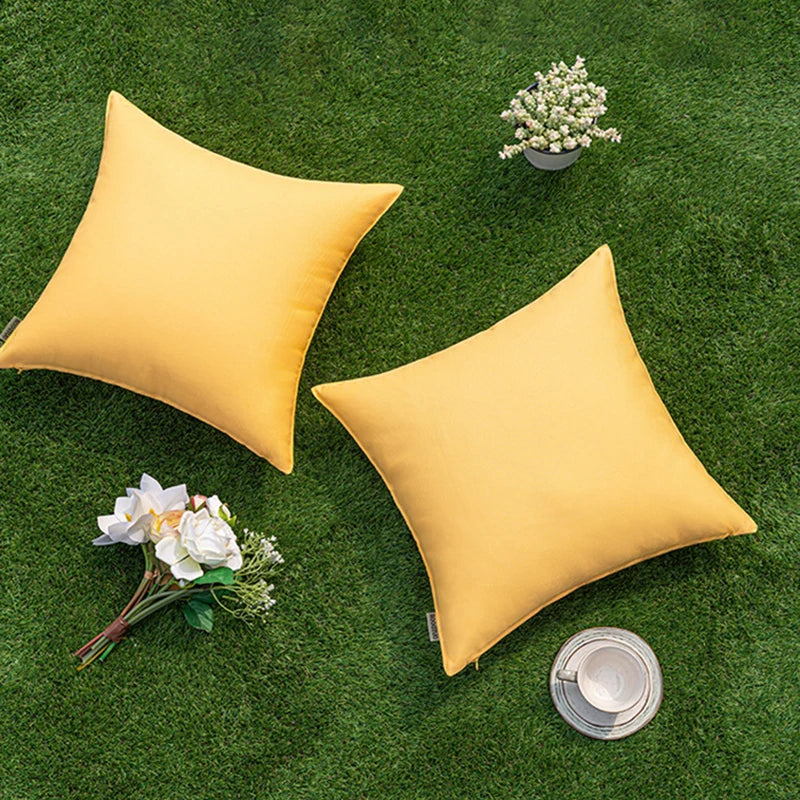 Housses de coussin extérieur imperméables, lot de 2 Nesty, deux housses jaune moutarde posées sur du gazon avec des fleurs blanches