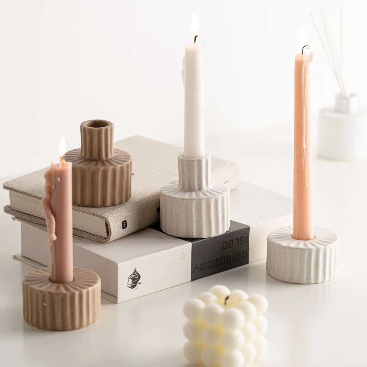 Bougeoirs céramique nordique godronnés en coloris brun, gris et blanc, avec bougies allumées, sur une pile de livres - Nesty