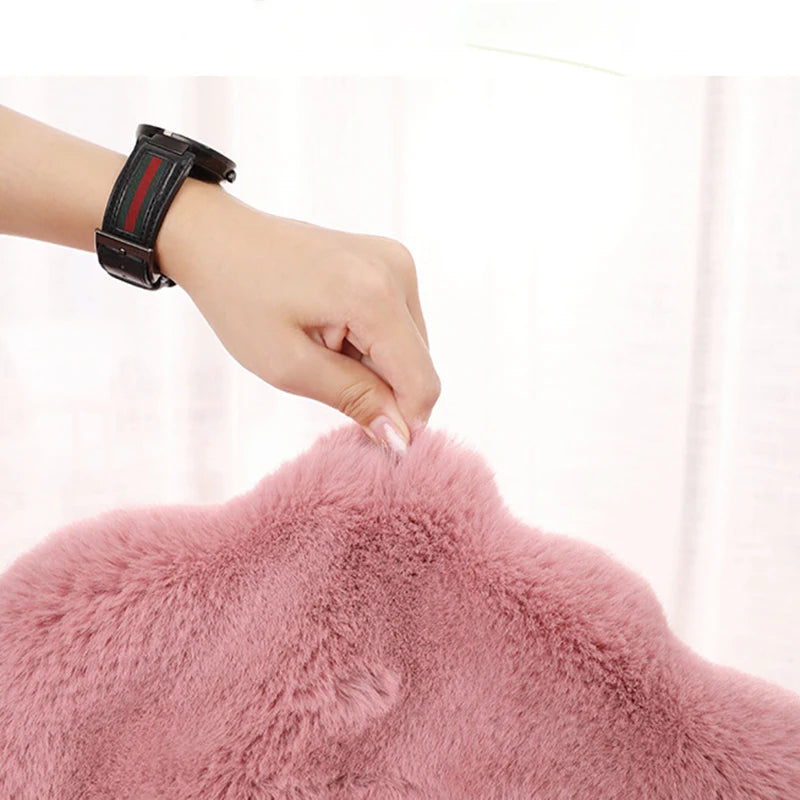 Tapis ovale en fausse fourrure douce Nesty - Chevet, gros plan sur une main effleurant le coloris rose poudré