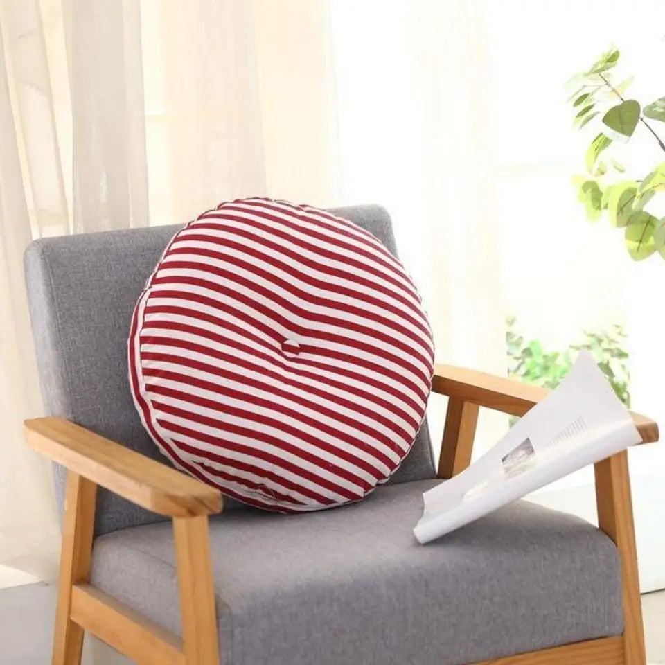 Grand coussin de méditation zafu en lin, pour banquette ou yoga Nesty, galette ronde à rayures rouges et blanches avec bouton central, posée sur fauteuil en bois à côté d'un magazine