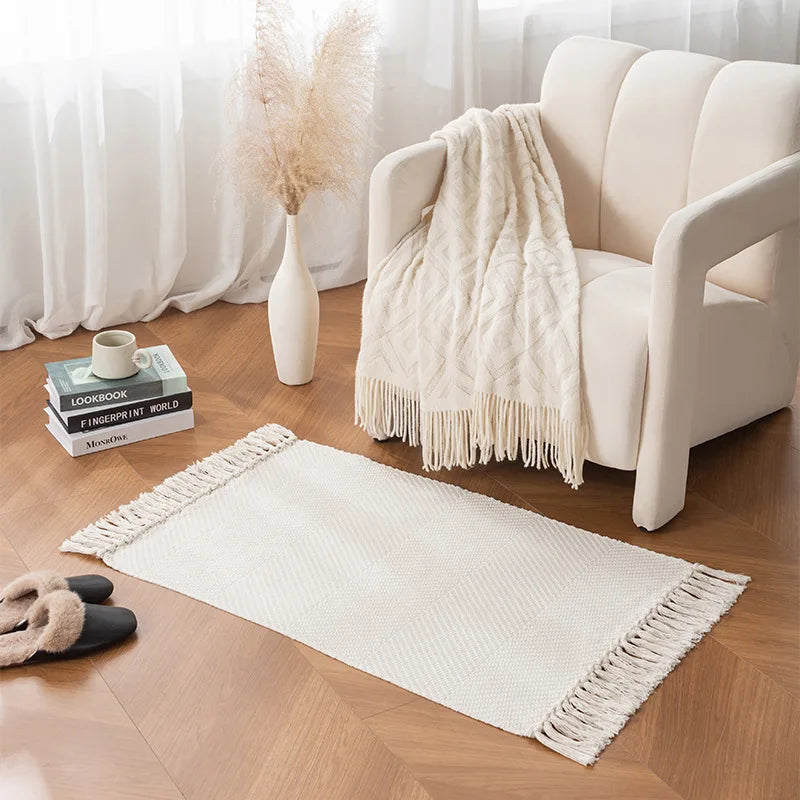 Tapis tressé en coton et lin — franges - Nesty, variante unie écrue texturée, posée près d'un fauteuil crème