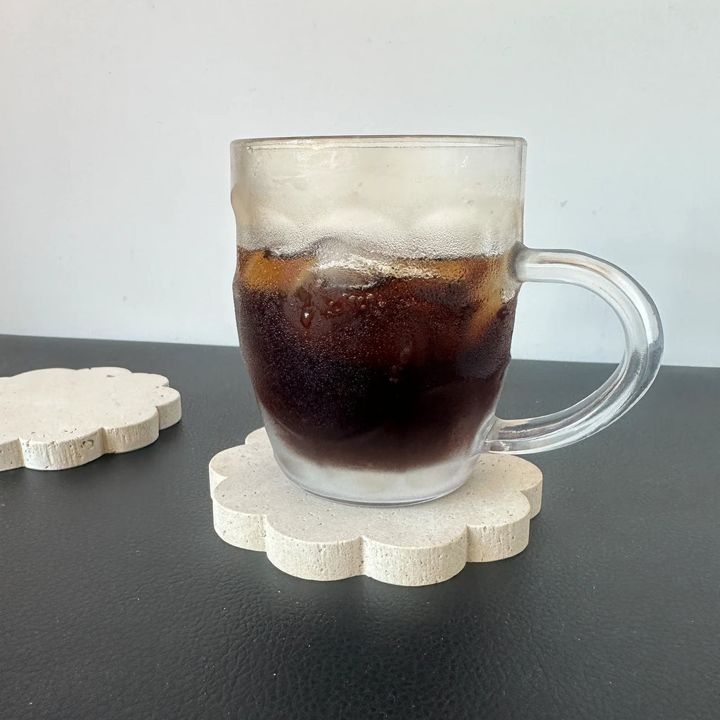 Dessous de verre en travertin, bord festonné, sous une tasse de café glacé sur table noire - Nesty