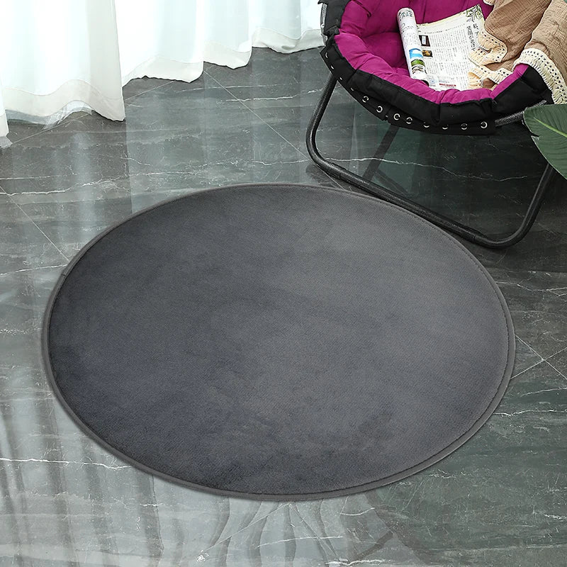 Petit tapis rond texturé gris foncé, posé au sol près d'un fauteuil suspendu à coussin magenta sur un sol en marbre.
