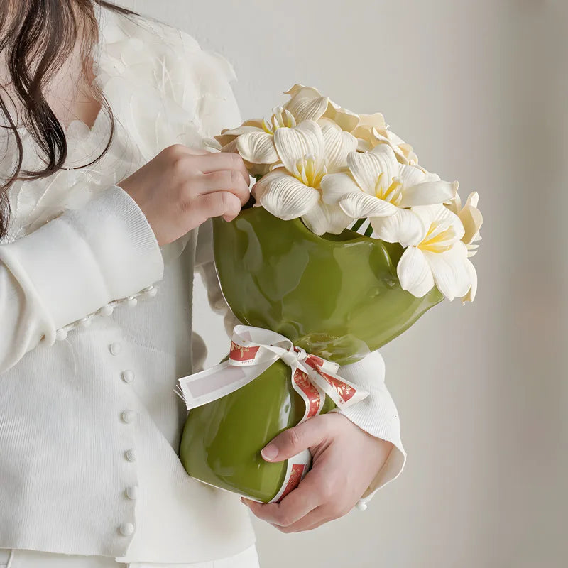 Vase en céramique en forme de rose, modèle bureau Nesty, vase céramique vert olive à col ondulé garni de fleurs blanches, tenu par une femme en tenue blanche