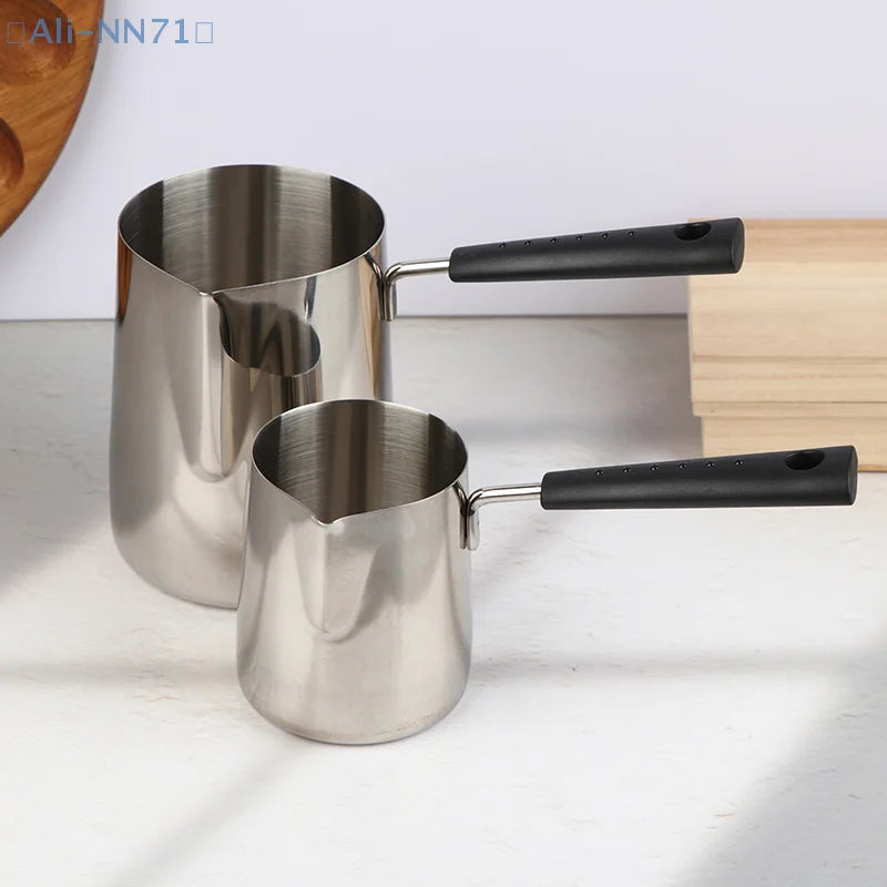 Casserole à manche long en inox pour lait et chocolat chaud Nesty, deux tailles à manche noir posées côte à côte sur table blanche, planche en bois à côté
