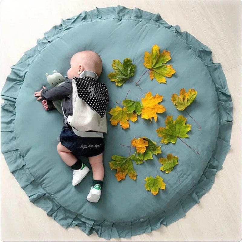 Tapis rond en coton pour bébé — coin jeux - Nesty, tapis rond vert-de-gris à bordure volantée, bébé allongé dessus entouré de feuilles d'automne