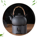 Chauffe-théière en céramique Nesty - Théière noire à anse en bambou posée sur le réchaud en céramique noire, fond sombre