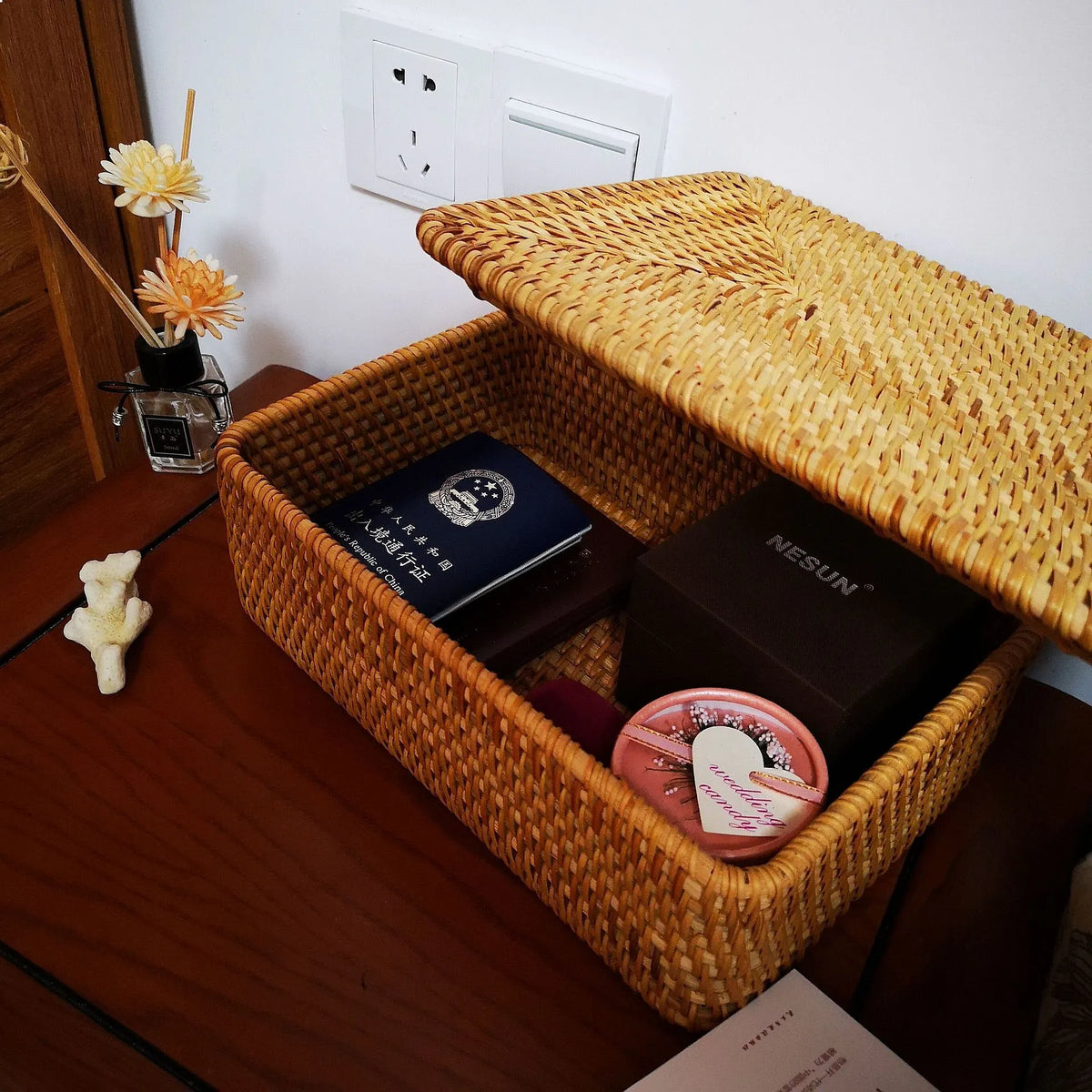 Boîte de rangement carrée en rotin tressé avec couvercle Nesty, boîte ouverte garnie d'un passeport, d'un écrin et d'un miroir de poche rose, couvercle relevé