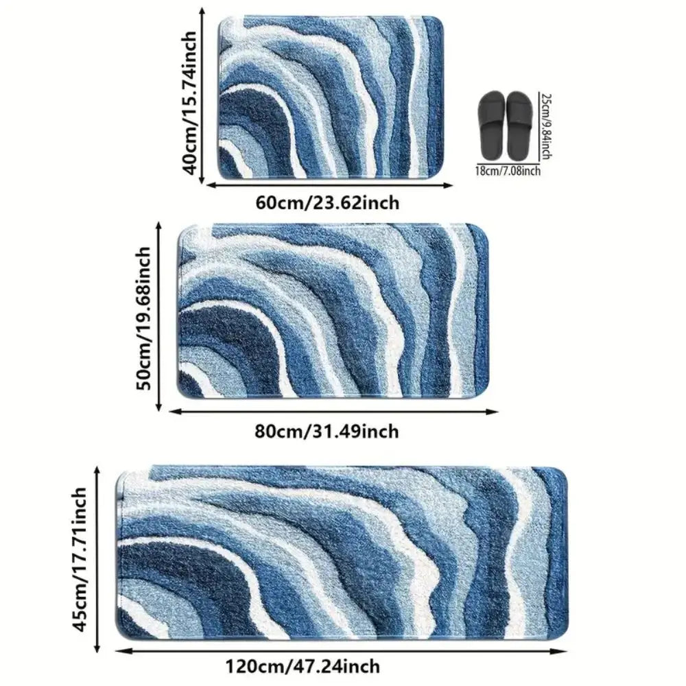 Trois tapis de bain à motif de vagues bleues de tailles différentes (60x40, 80x50 et 120x45 cm), avec une paire de chaussons pour l'échelle.