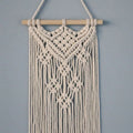 Tenture macramé en coton à esprit bohème Nesty, tenture triangulaire blanche à motif de losanges noués, suspendue sur un mur gris-bleu