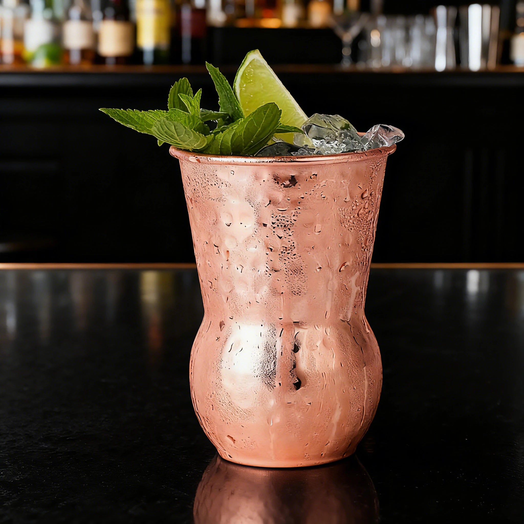 Gobelet tiki en inox cuivré, 350ml Nesty, martelé cuivré garni de glaçons, menthe et quartier de citron vert, sur bar sombre