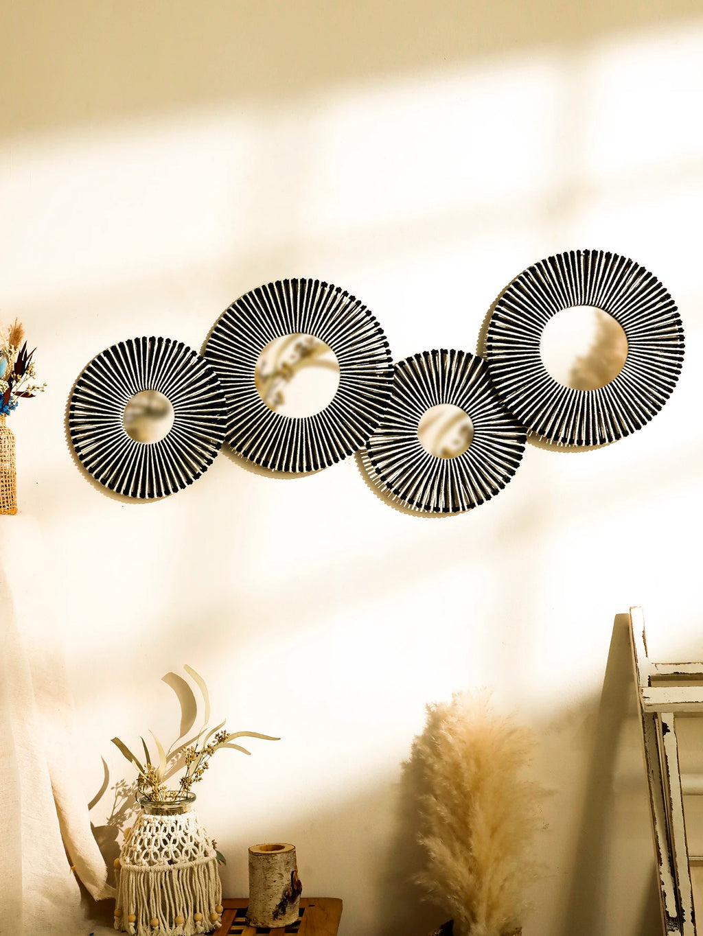 Ensemble de 4 miroirs muraux ronds en corde tressée façon soleil, coloris noir et blanc, sur un mur ensoleillé avec pampas - Nesty