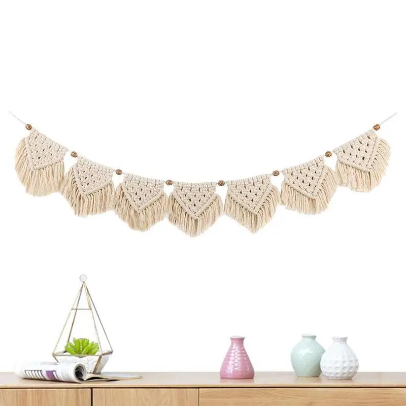 Tenture macramé à franges à tissage bohème Nesty, guirlande sur fond blanc, posée au-dessus d'un meuble avec petits vases