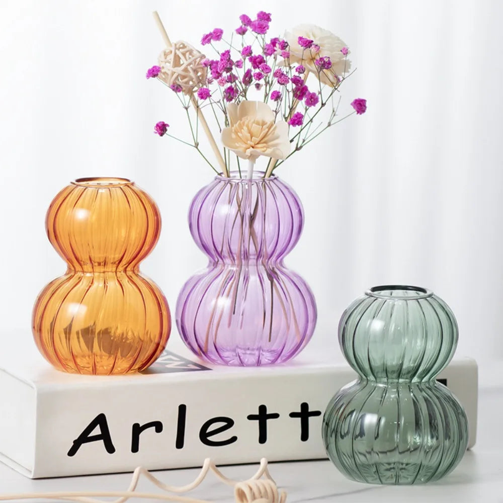 Vase en verre forme calebasse, rayures verticales - Nesty - Trois coloris ambre, violet et vert sauge posés sur un livre, le violet garni de fleurs stabilisées roses et blanches
