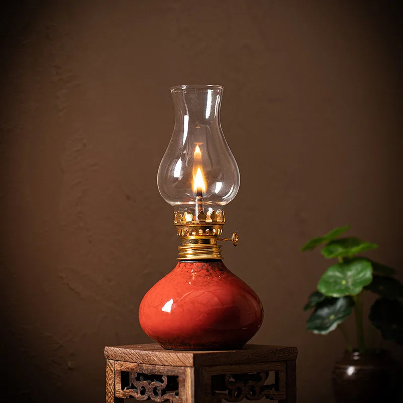 Lampe à huile en céramique Nesty - Lampe à huile rouge allumée avec globe en verre, posée sur un socle en bois sculpté près d'une plante verte