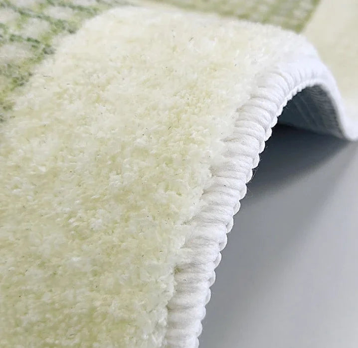 Gros plan sur le bord d'un tapis vert et crème, montrant la bordure cousue en blanc.