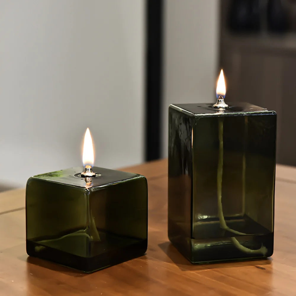 Lampe à huile en verre vert Nesty - Deux lampes cubiques allumées, gros plan sur une table en bois
