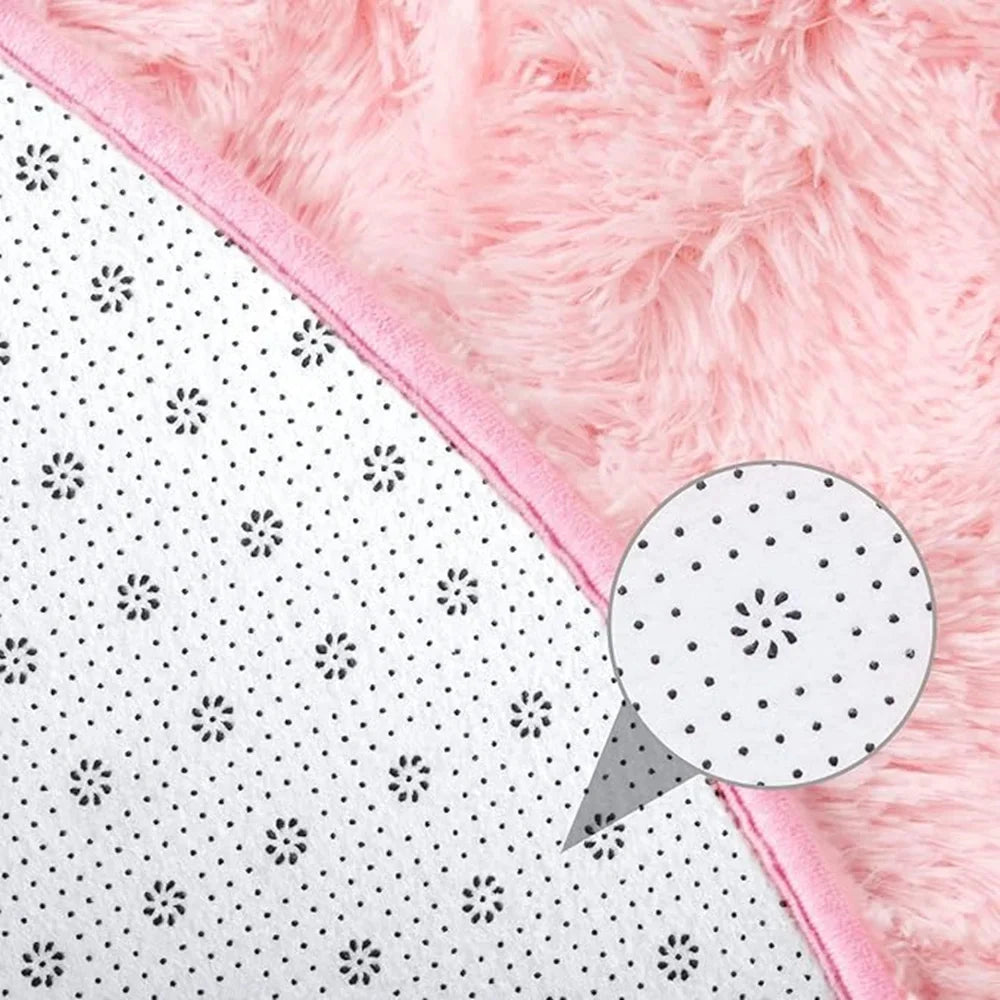 Gros plan sur le bord d'un tapis en fausse fourrure rose, montrant l'envers antidérapant à motif de pois.