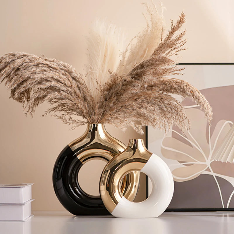 Vase en céramique doré, silhouette nordique, plusieurs tailles Nesty, deux vases ronds ajourés bicolores noir et doré garnis de plumes de pampa, sur une table blanche
