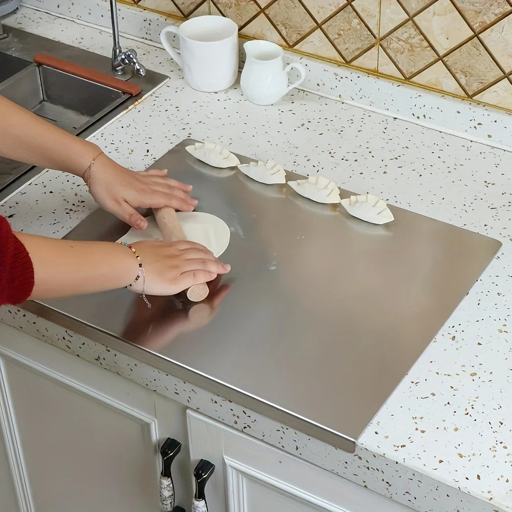 Planche à découper en acier inoxydable, antidérapante Nesty, mains étalant de la pâte au rouleau à côté de raviolis pliés, planche en acier fixée au bord d'un évier