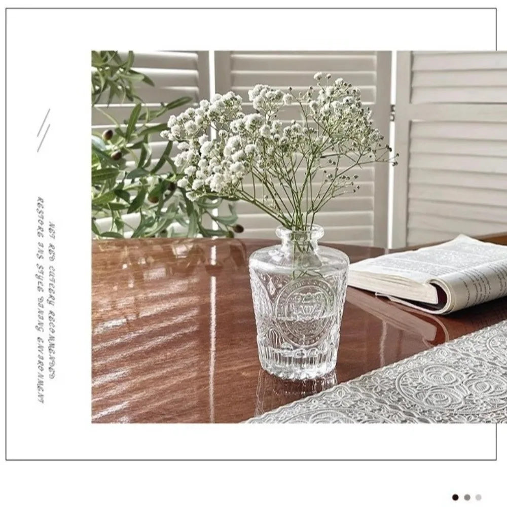 Set de mini vases en verre transparent, motif en relief - Nesty - Vase à motif gravé avec brins de gypsophile blanche, posé sur une table en bois sombre près d'un livre ouvert