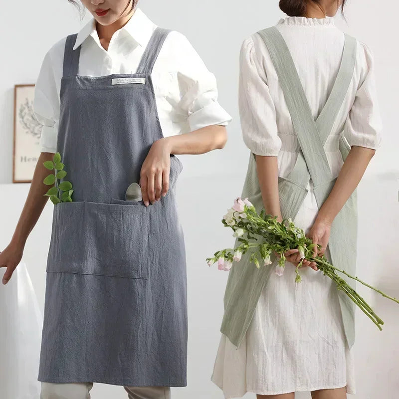 Deux modèles portant le tablier en lin, l'un gris de face avec brin d'eucalyptus, l'autre vert clair de dos avec un bouquet de fleurs - Nesty