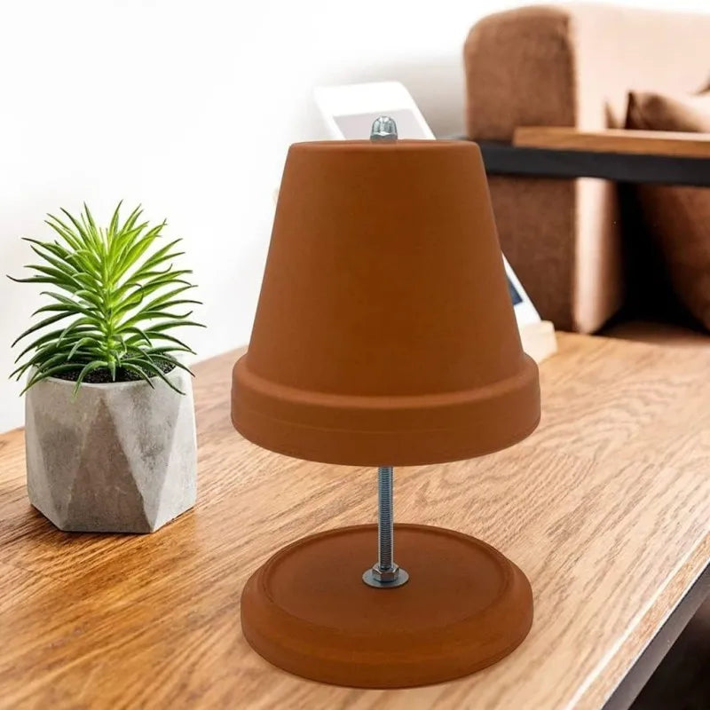 Chauffe-plat en terre cuite Nesty - Lampe chauffe-plat en pot de terre cuite renversé sur pied métallique, posée sur une table en bois avec une plante